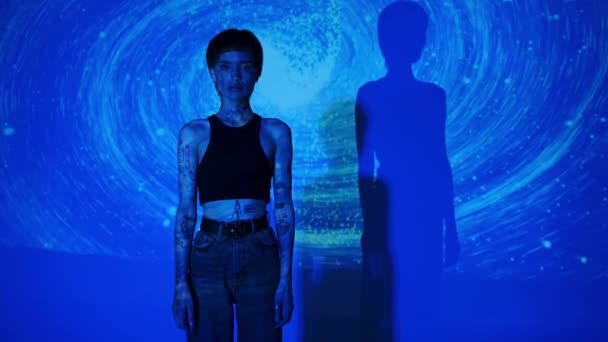 Татуированная женщина смотрит в камеру на абстрактном синем фоне  - Кадры, видео