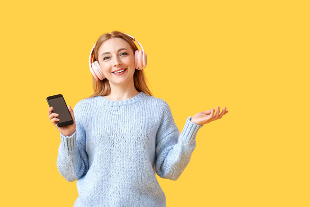 Mature woman with headphones and mobile phone on color background - Photo, Image