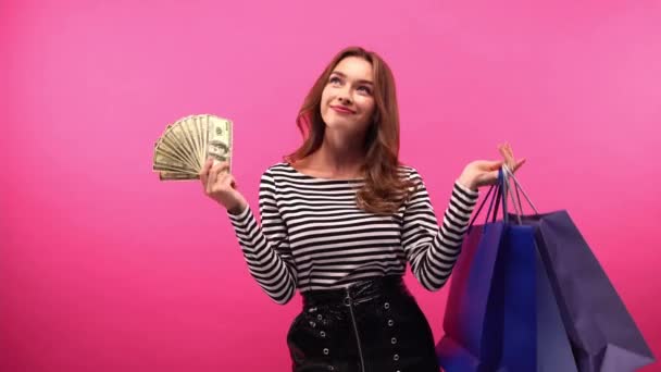 mujer feliz sosteniendo bolsas de compras y dólares aislados en rosa - Metraje, vídeo