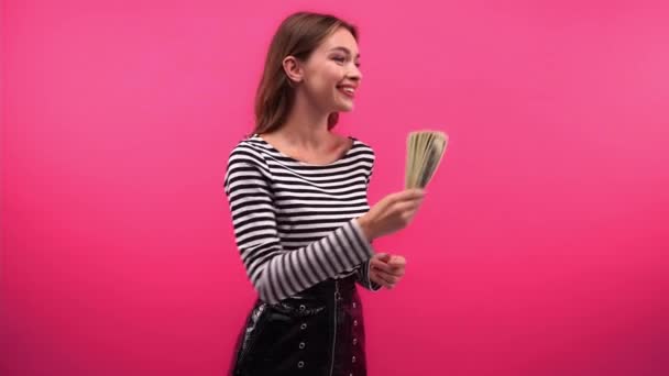 felice donna con dollari prendendo shopping bags da uomo isolato su rosa - Filmati, video