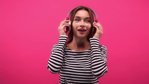 ευχαριστημένη γυναίκα που βάζει ακουστικά και ακούει μουσική απομονωμένη σε ροζ - Πλάνα, βίντεο
