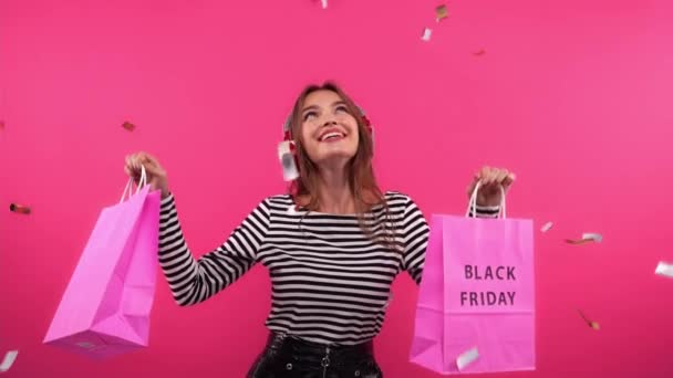 счастливая женщина танцует с сумками под конфетти на розовом - Кадры, видео