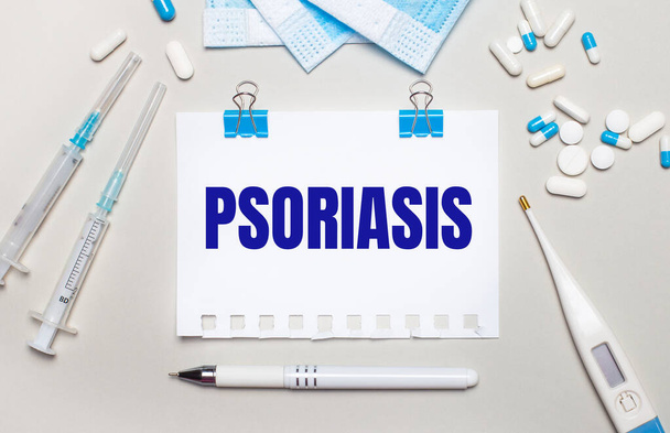 On a light gray background, blue medical masks, syringes, an electronic thermometer, pills, a pen and a notebook with the inscription PSORIASIS. Medical concept - Fotó, kép
