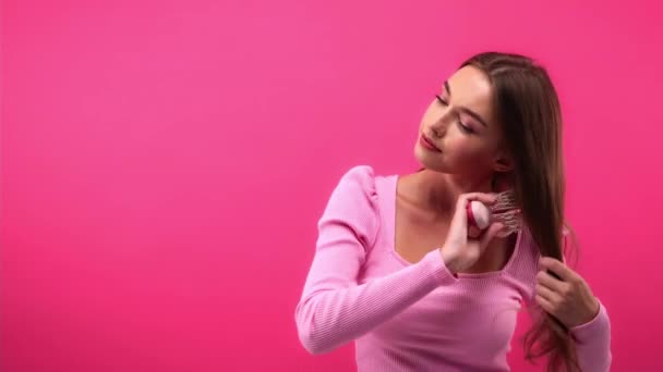 mujer joven cepillando el cabello aislado en rosa - Metraje, vídeo