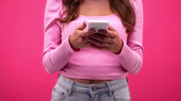 καλλιεργημένη άποψη της γυναίκας που χρησιμοποιεί κινητό τηλέφωνο απομονωμένο σε ροζ - Πλάνα, βίντεο