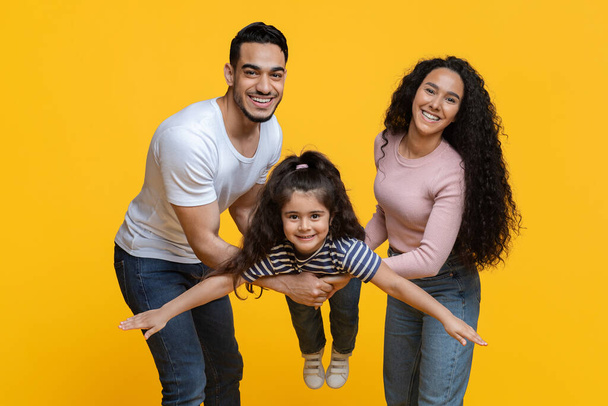 Family Fun. Cheerful Middle-Eastern Mom And Dad Playing With Their Little Daughter - 写真・画像