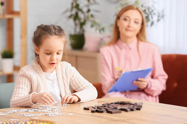 Маленька дівчинка з аутичним розладом складання головоломки в кабінеті дитячого психолога
 - Фото, зображення