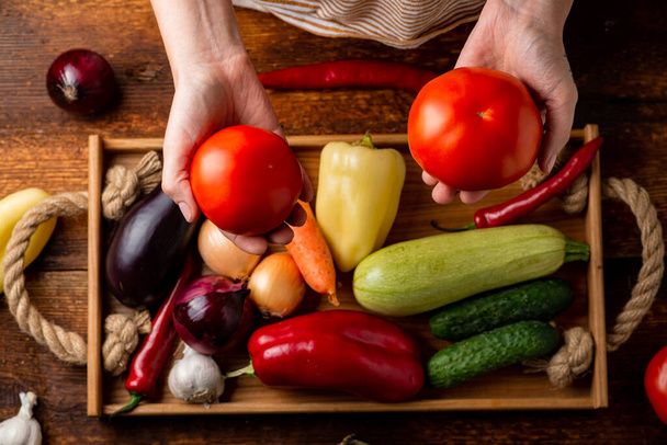 Eine nicht wiedererkennbare Frau hält eine Tomate auf einem Hintergrund aus verschiedenen Gemüsesorten. Das Konzept der gesunden Ernährung, Vegetarismus. - Foto, Bild
