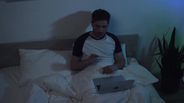 Zeitlupe: Mann zeigt mit Finger während Videochat auf Laptop im Bett - Filmmaterial, Video