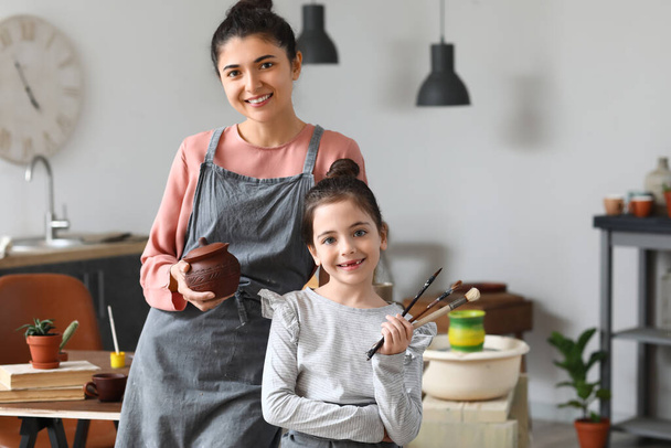 Bambina e sua madre con pennelli e pentola in ceramica a casa - Foto, immagini