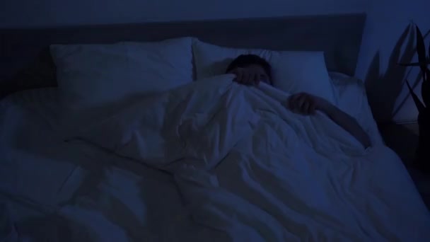 verängstigter Mann versteckt sich mit Blaulicht unter Decke im Schlafzimmer - Filmmaterial, Video