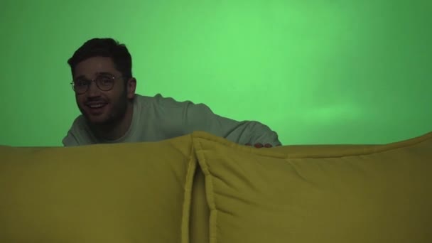hombre juguetón en anteojos mirando hacia fuera sofá en verde - Metraje, vídeo