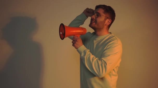 man pointing with finger and shouting in megaphone on grey with lighting - Footage, Video