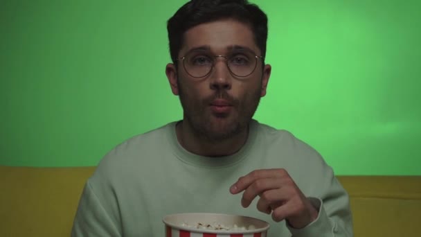 pozitív férfi hányás és eszik popcorn, miközben filmet néz a zöld - Felvétel, videó