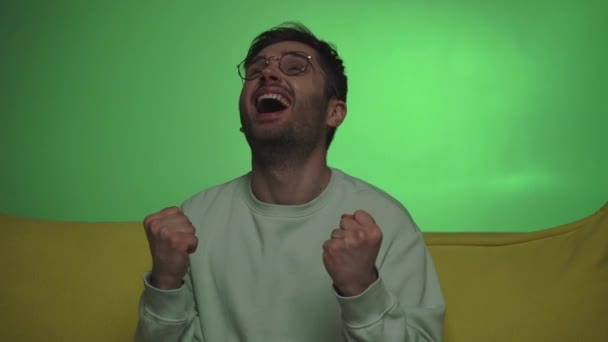 podekscytowany mężczyzna w okularach pokazując gest wygranej podczas oglądania telewizji na zielono - Materiał filmowy, wideo