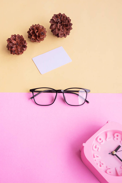 квадратні окуляри, будильник, квіти соснового дерева на пастельному рожевому та пастельно-жовтому тлі. Літня концепція, мінімальна концепція
 - Фото, зображення