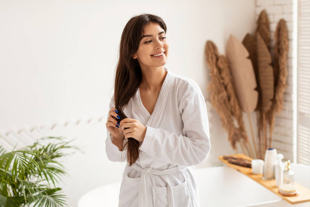 Привлекательная брюнетка леди, ухаживающая за длинными прямыми волосами в ванной комнате - Фото, изображение
