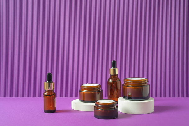 Amber glazen flessen en potten met trendy geometrische vormen op een violette achtergrond. - Foto, afbeelding