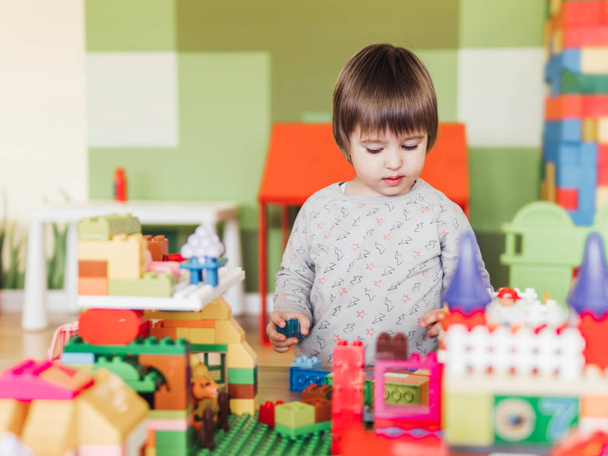 Toddler boy is playing in kidsroom with colorful constructor. Educational toy block in his hands. Kid is busy with toy bricks. - Foto, afbeelding