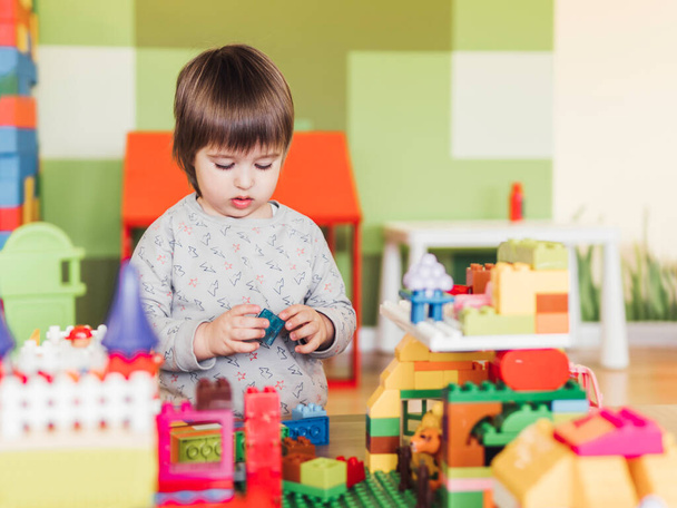 Toddler boy is playing in kidsroom with colorful constructor. Educational toy block in his hands. Kid is busy with toy bricks. - Photo, Image