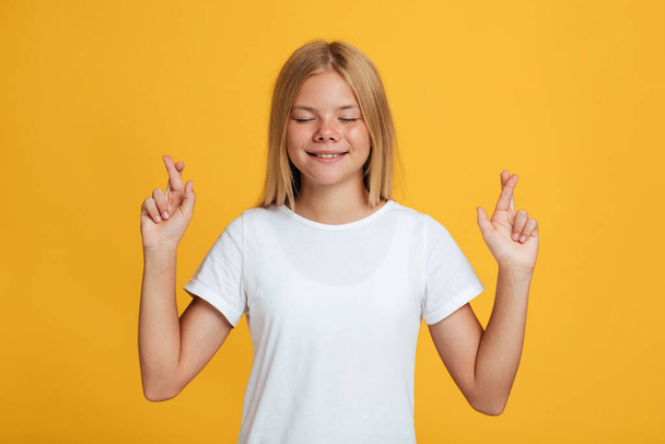 gelukkig schattig adolescent Kaukasisch blond meisje met gesloten ogen verhogen gekruiste vingers en wens - Foto, afbeelding