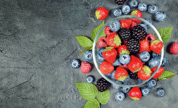 berries of raspberries, strawberries, blackberries and blueberries in a plate on a concrete table, top view - Foto, Imagem
