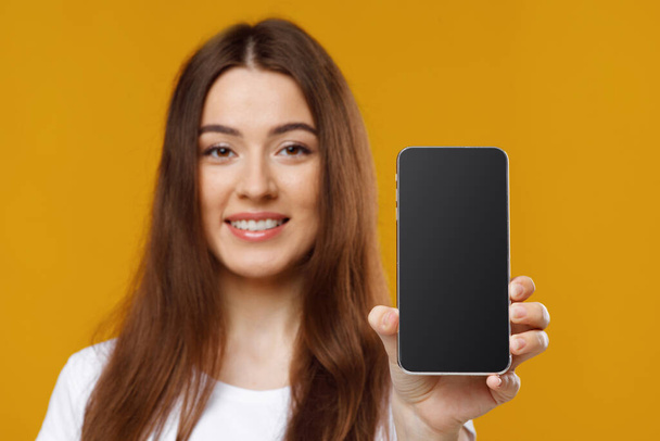 Nahaufnahme der schönen jungen Frau zeigt Handy mit leerem Bildschirm - Foto, Bild