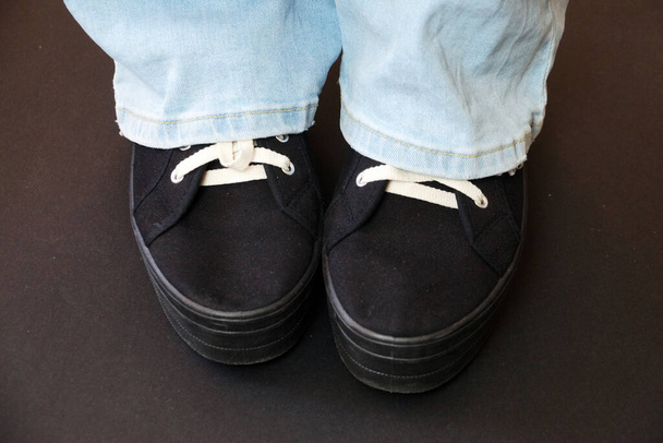 женские ноги в синих джинсах и черных кроссовках на черном фоне. - Фото, изображение