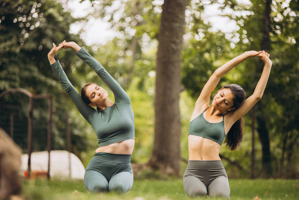 Dos hermosas mujeres jóvenes haciendo yoga y ejercicios de estiramiento al aire libre en el cálido día de verano - Foto, Imagen