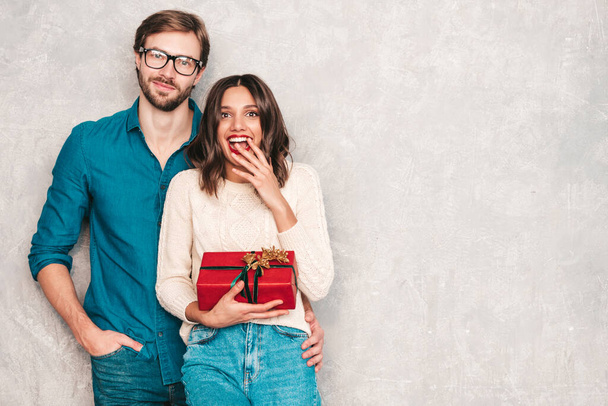 Smiling beautiful woman and her handsome boyfriend. Happy cheerful family posing in studio near gray wall. Valentine's Day. Models hugging and giving his girlfriend gift box. Christmas, x-mas, concept - Photo, image