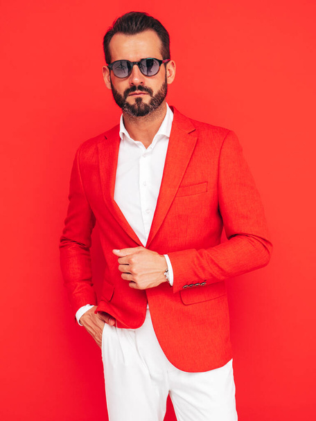 Portrait of handsome confident stylish hipster lambersexual model. Sexy modern man dressed in elegant suit. Fashion male posing in studio near red wall in sunglasses - Foto, Bild