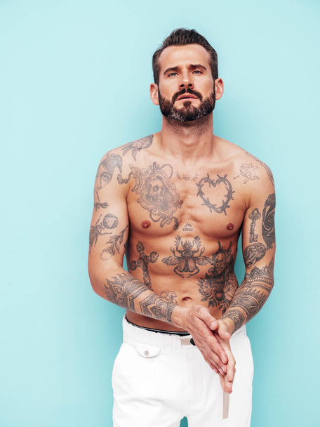 Portrait of handsome confident stylish hipster lambersexual model. Sexy modern man. Naked torso with tattoos.Fashion male posing in studio near light blue wall - Фото, изображение