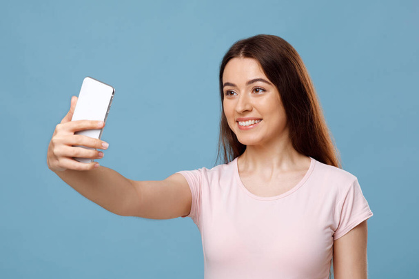 Houkutteleva nuori nainen ottaa selfie sininen studio tausta - Valokuva, kuva