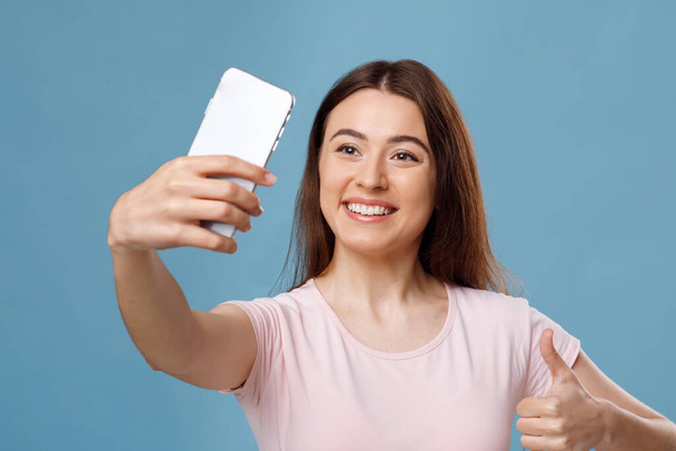 Smiling fair-haired young woman taking selfie on smartphone, closeup - 写真・画像