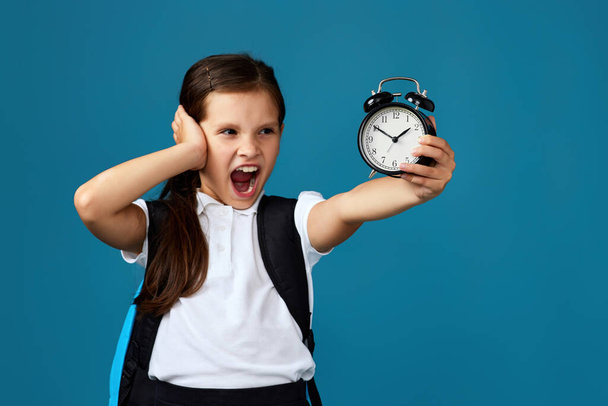 schoolgirl with backpack is holding alarm clock - Foto, imagen