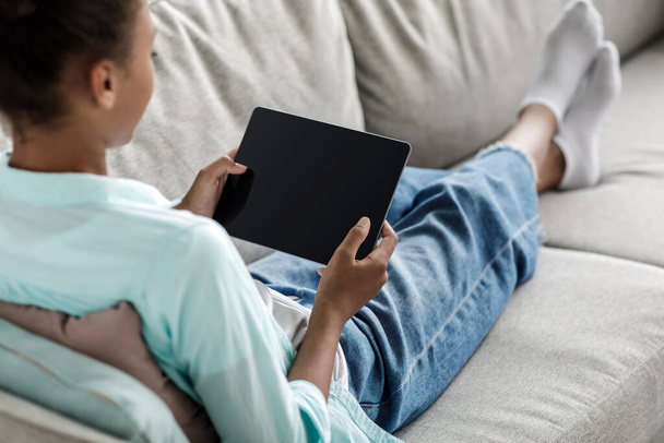 Подростковая африканская девочка-ученица набирает текст на планшете с чистым экраном и учится дома - Фото, изображение