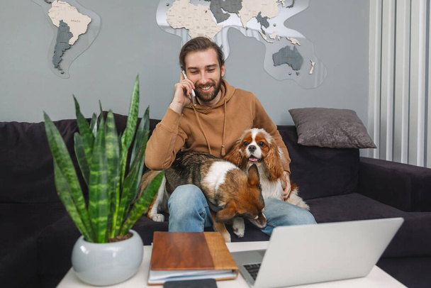 Young handsome man talking on cell phone at home and hugging his dogs - Photo, Image