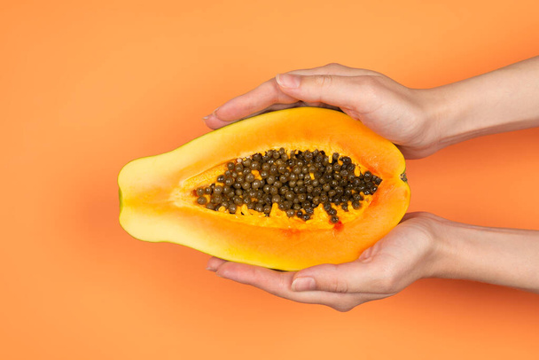 Παπάγια φρούτα σε πορτοκαλί φόντο σε γυναικεία χέρια. Μισή παπάγια. - Φωτογραφία, εικόνα