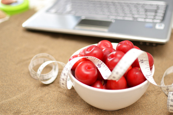 Ciruelas rojas, laptop y cinta métrica en arena
 - Foto, Imagen