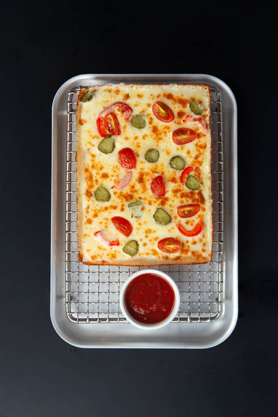 Detroit pizza op een ijzeren dienblad met saus op een donkere achtergrond. selectieve focus. - Foto, afbeelding