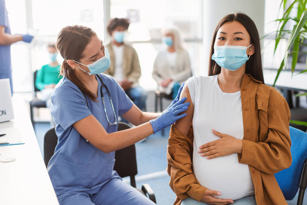 Беременная женщина с Асином получает вакцину против ковида-19, доктор применяет гипс - Фото, изображение