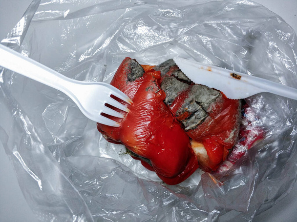 Пластиковый нож и вилка застряли в испорченном красном перце в пакете. Плесень. Избыточное потребление. - Фото, изображение