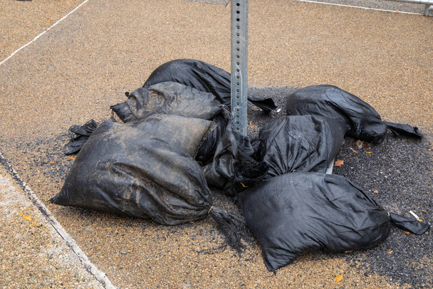 Zwarte geweven plastic zakken gevuld met asfalt slakken ter ondersteuning van de basis van een tijdelijke straatnaambord, geaggregeerde stoep, horizontaal aspect - Foto, afbeelding