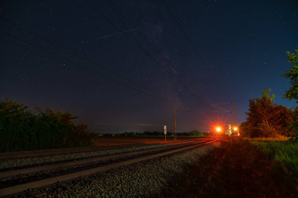 Voie lactée avec son centre galactique au-dessus d'une voie ferrée isolée se tenant au-dessus du signal du train d'arrêt lors d'une nuit étoilée. - Photo, image