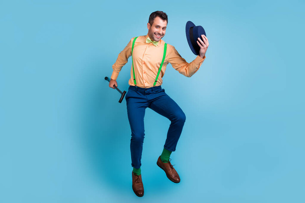 Profile photo of cheerful guy jump hold cane take off hat wear suspenders shirt bow tie isolated blue color background - Fotografie, Obrázek