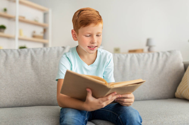 Cute redhead boy sitting at home, reading book - Photo, Image
