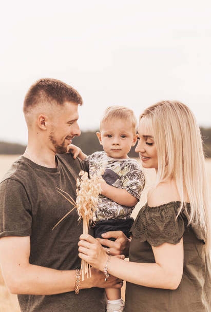 Beautiful family parents and a young son in a wheat field. Mom, Dad and Baby Together. Happy family, parents hugs their little son - 写真・画像