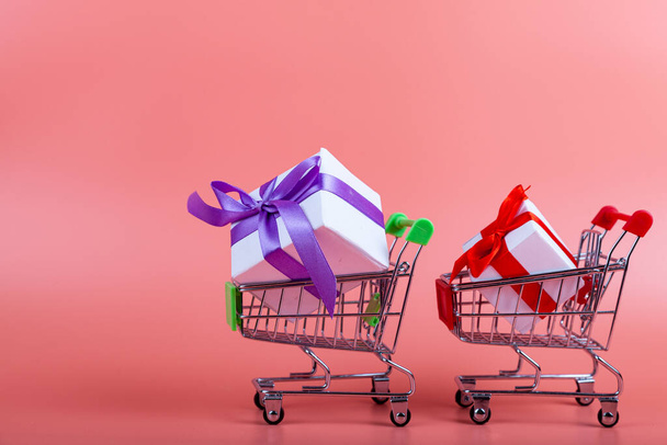 Shopping cart and gifts on a pink background. Concept: buying gifts. - Fotoğraf, Görsel