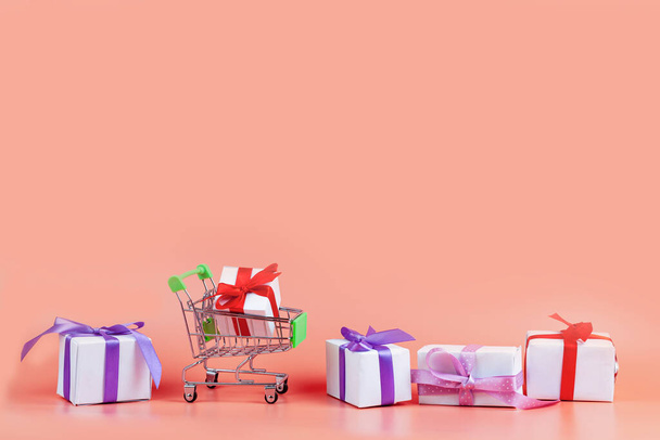 Nákupní košík a dárky na růžovém pozadí. Koncept: nákup dárky. - Fotografie, Obrázek