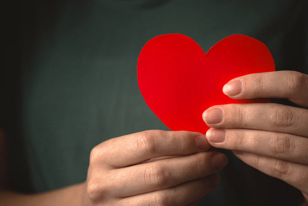 Close-up to red heart in hands. Woman holding paper heart on her chest background  - Foto, imagen